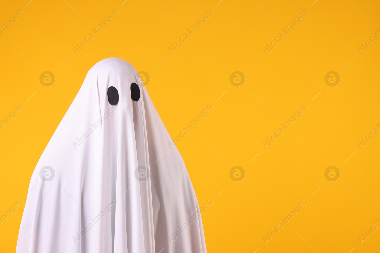 Photo of Creepy ghost. Man covered with white sheet on orange background. Space for text