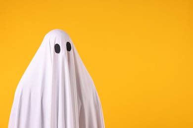 Photo of Creepy ghost. Man covered with white sheet on orange background. Space for text