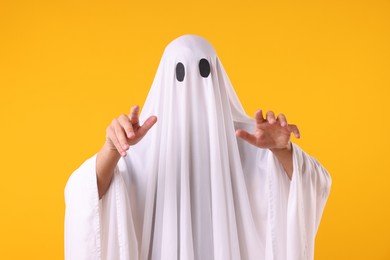 Photo of Creepy ghost. Man covered with white sheet on orange background