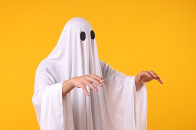 Photo of Creepy ghost. Man covered with white sheet on orange background