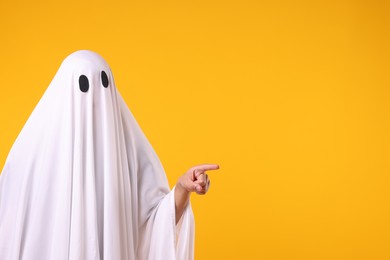 Photo of Man in ghost costume pointing at something on orange background. Space for text