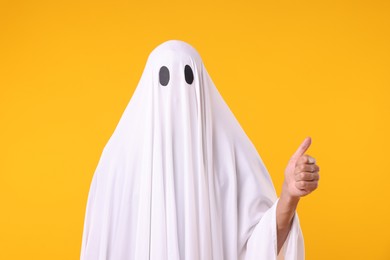 Photo of Man in ghost costume showing thumbs up on orange background