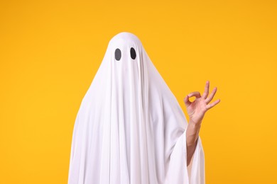 Photo of Man in ghost costume showing OK gesture on orange background