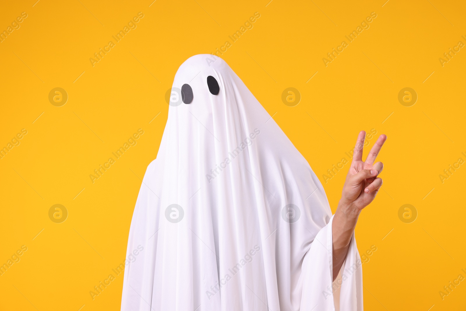Photo of Man in ghost costume showing V-sign on orange background