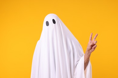Photo of Man in ghost costume showing V-sign on orange background