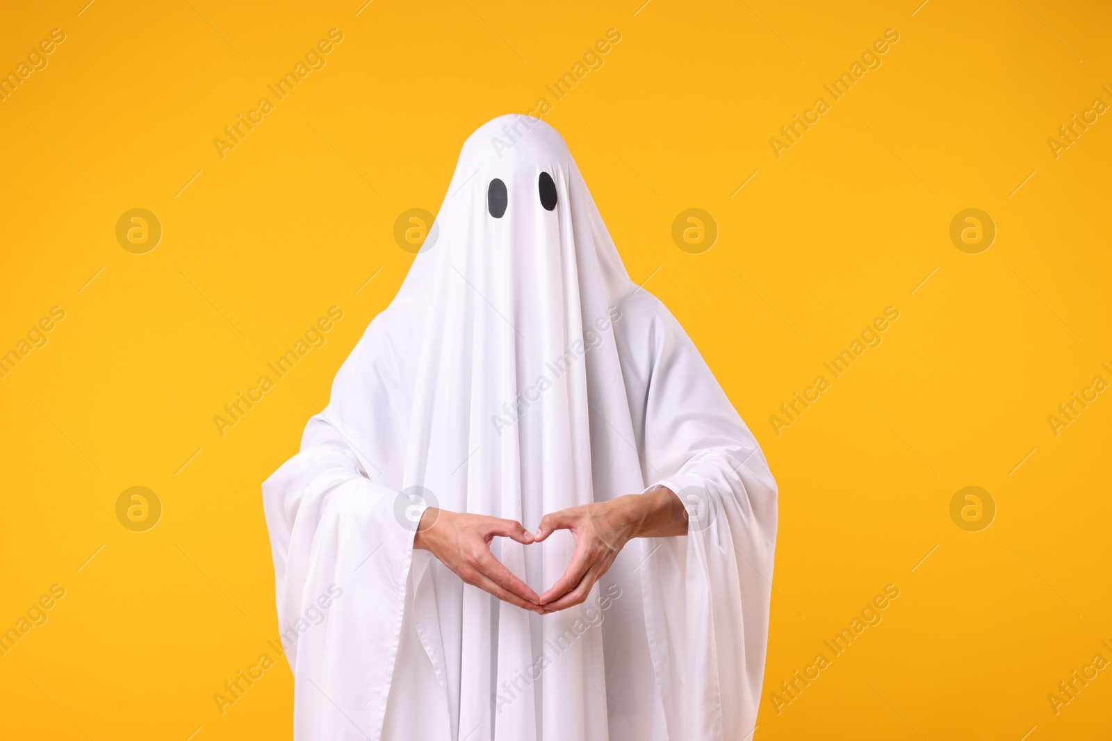 Man in ghost costume making heart gesture with hands on orange background Photo of Man in ghost costume making heart gesture with hands on orange background