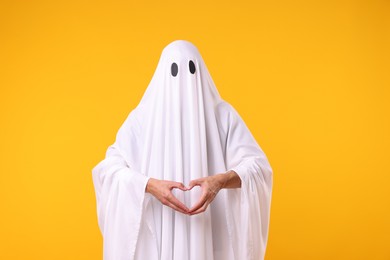 Photo of Man in ghost costume making heart gesture with hands on orange background