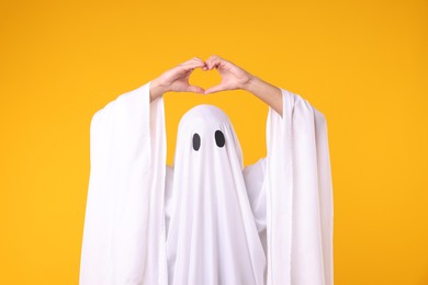 Photo of Man in ghost costume making heart gesture with hands on orange background