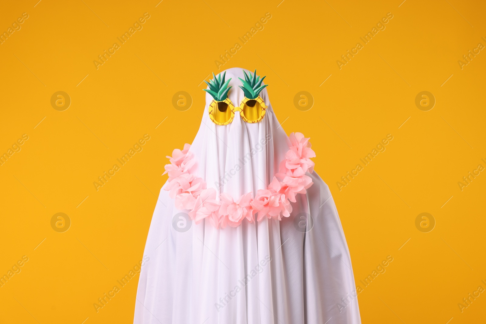 Funny ghost. Man covered with white sheet in sunglasses and wreath of flowers on orange background Photo of Funny ghost. Man covered with white sheet in sunglasses and wreath of flowers on orange background