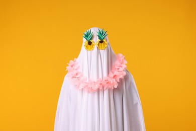 Photo of Funny ghost. Man covered with white sheet in sunglasses and wreath of flowers on orange background