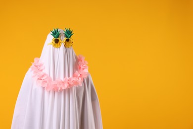 Photo of Funny ghost. Man covered with white sheet in sunglasses and wreath of flowers on orange background, space for text