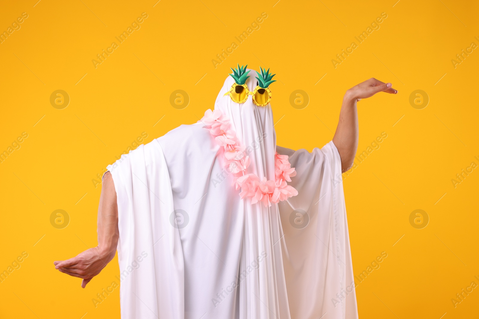 Funny ghost. Man covered with white sheet in sunglasses and wreath of flowers dancing on orange background Photo of Funny ghost. Man covered with white sheet in sunglasses and wreath of flowers dancing on orange background