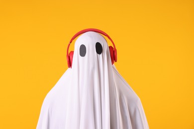 Photo of Man in ghost costume wearing headphones on orange background