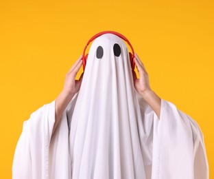 Photo of Man in ghost costume wearing headphones on orange background