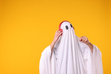 Photo of Man in ghost costume wearing headphones on orange background. Space for text