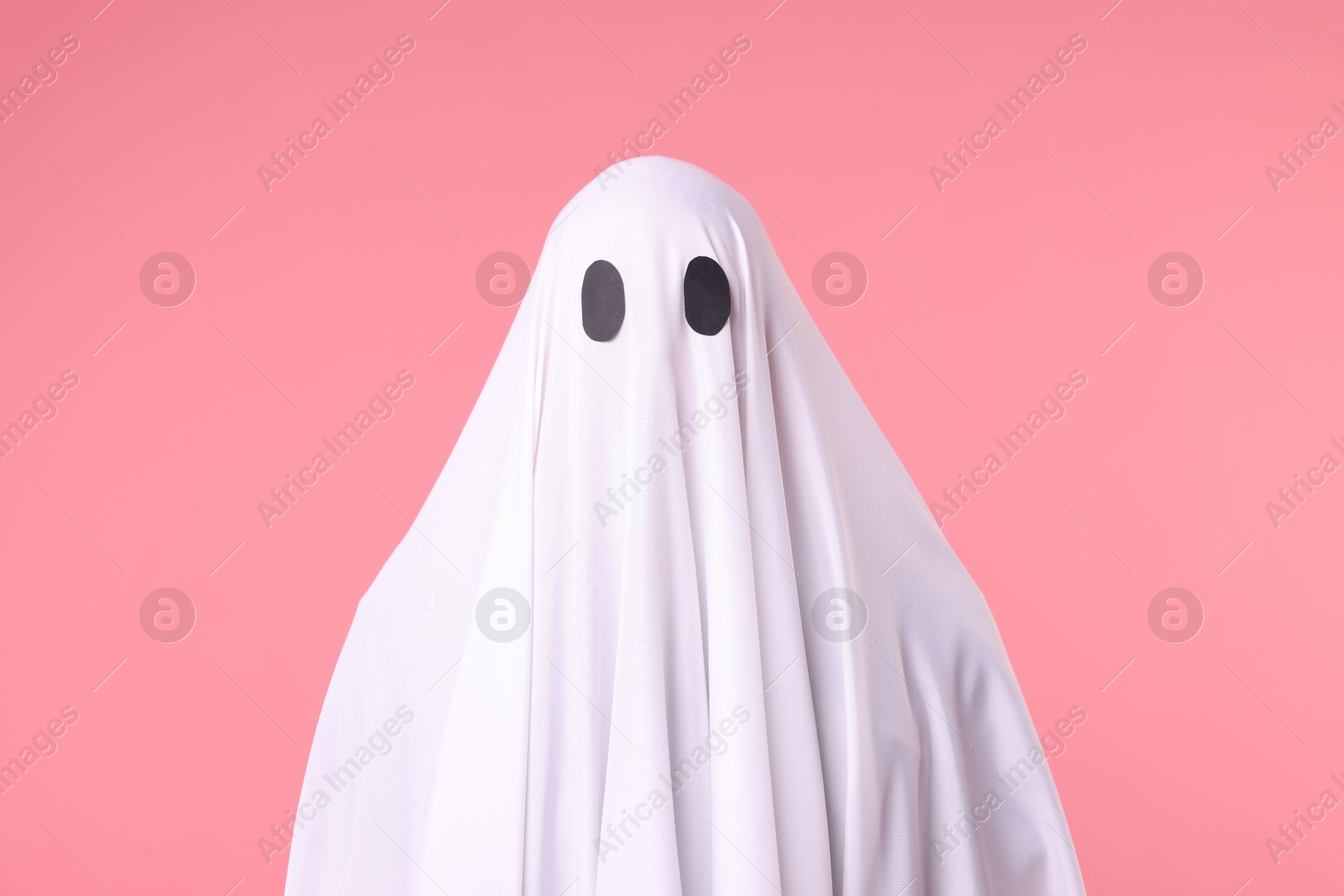 Creepy ghost. Man covered with white sheet on pink background Photo of Creepy ghost. Man covered with white sheet on pink background