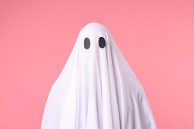 Photo of Creepy ghost. Man covered with white sheet on pink background