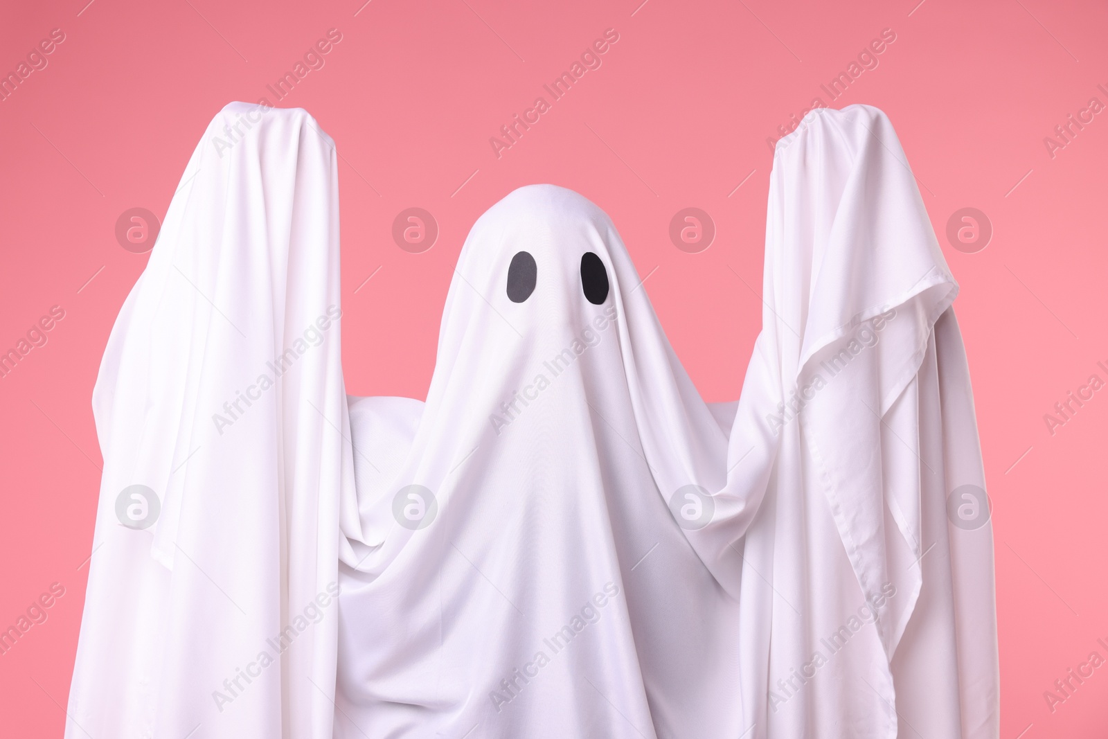 Creepy ghost. Man covered with white sheet on pink background Photo of Creepy ghost. Man covered with white sheet on pink background