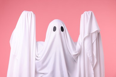 Photo of Creepy ghost. Man covered with white sheet on pink background