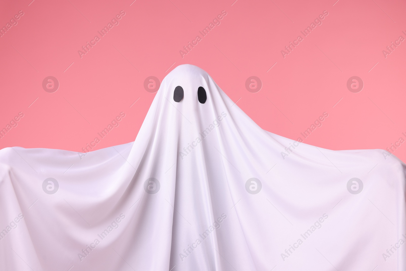 Creepy ghost. Man covered with white sheet on pink background Photo of Creepy ghost. Man covered with white sheet on pink background