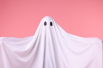 Photo of Creepy ghost. Man covered with white sheet on pink background
