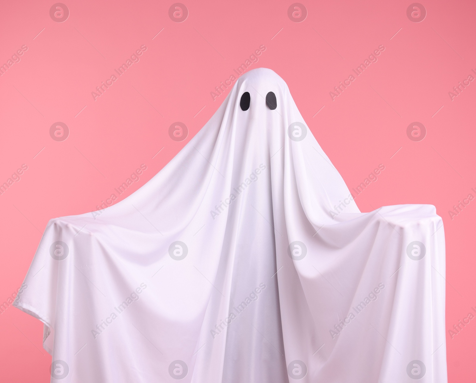 Creepy ghost. Man covered with white sheet on pink background Photo of Creepy ghost. Man covered with white sheet on pink background