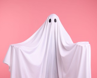 Photo of Creepy ghost. Man covered with white sheet on pink background