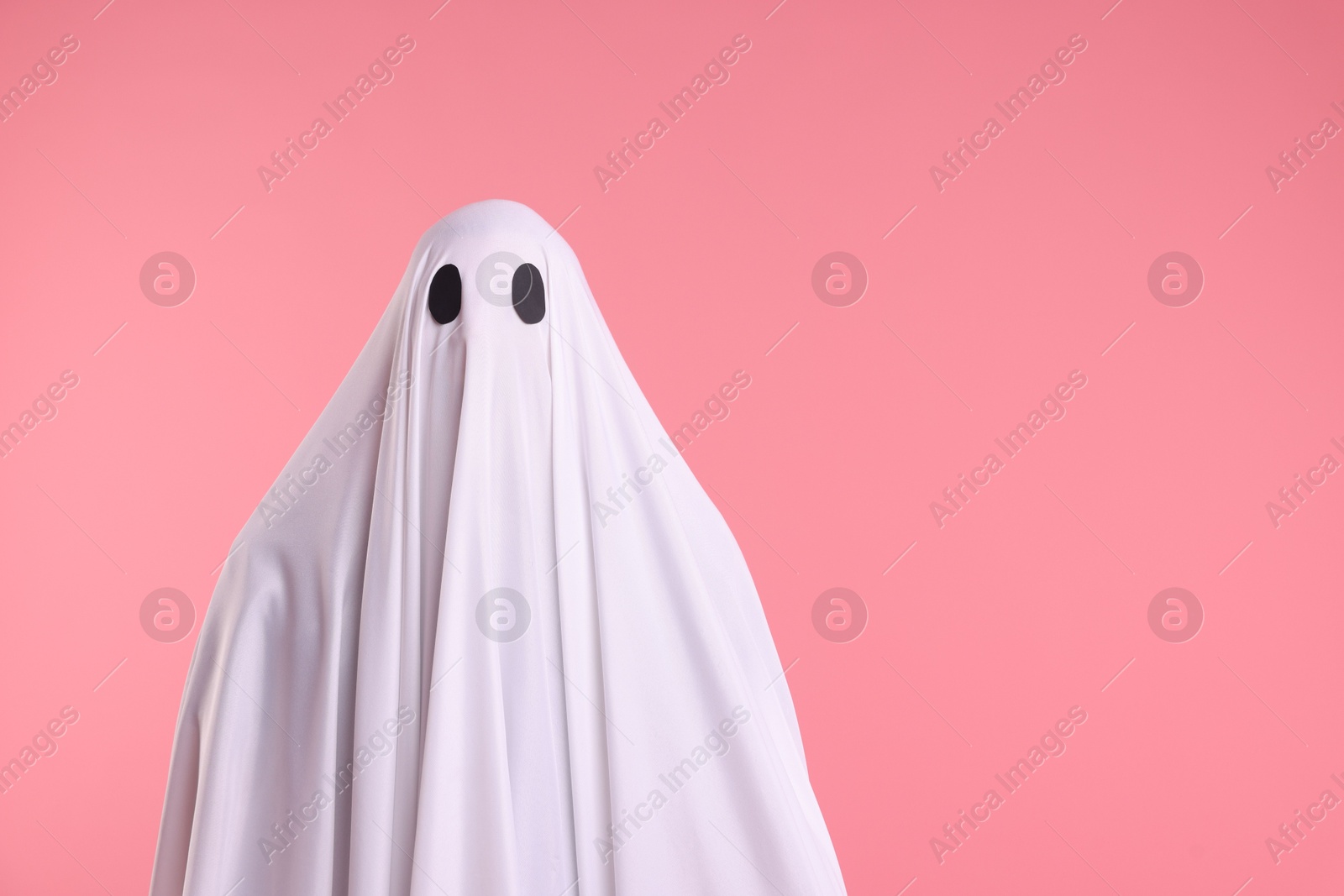 Creepy ghost. Man covered with white sheet on pink background. Space for text Photo of Creepy ghost. Man covered with white sheet on pink background. Space for text