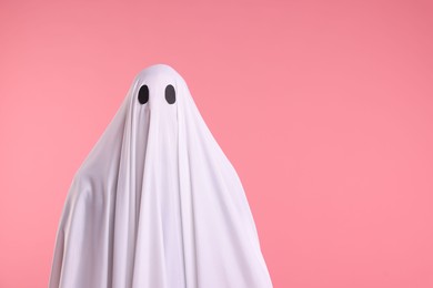 Photo of Creepy ghost. Man covered with white sheet on pink background. Space for text