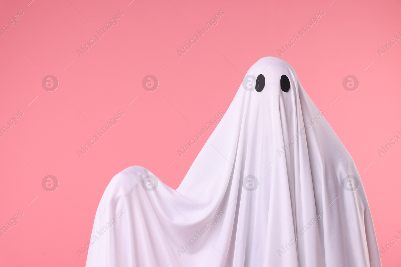 Creepy ghost. Man covered with white sheet on pink background. Space for text Photo of Creepy ghost. Man covered with white sheet on pink background. Space for text