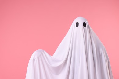 Photo of Creepy ghost. Man covered with white sheet on pink background. Space for text