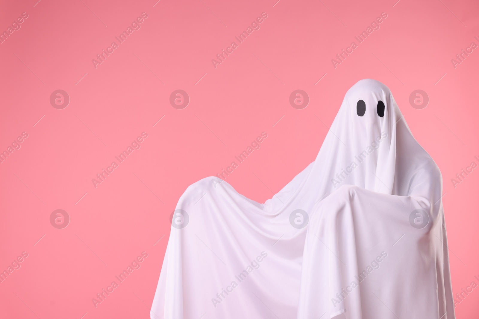 Creepy ghost. Man covered with white sheet on pink background. Space for text Photo of Creepy ghost. Man covered with white sheet on pink background. Space for text