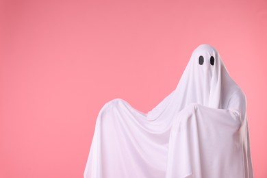 Photo of Creepy ghost. Man covered with white sheet on pink background. Space for text