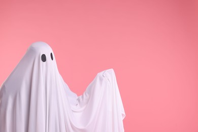 Photo of Creepy ghost. Man covered with white sheet on pink background. Space for text