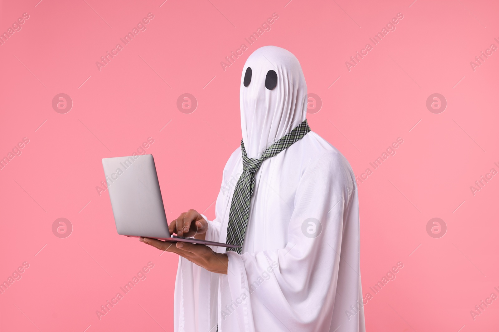 Photo of Man in ghost costume using laptop on pink background
