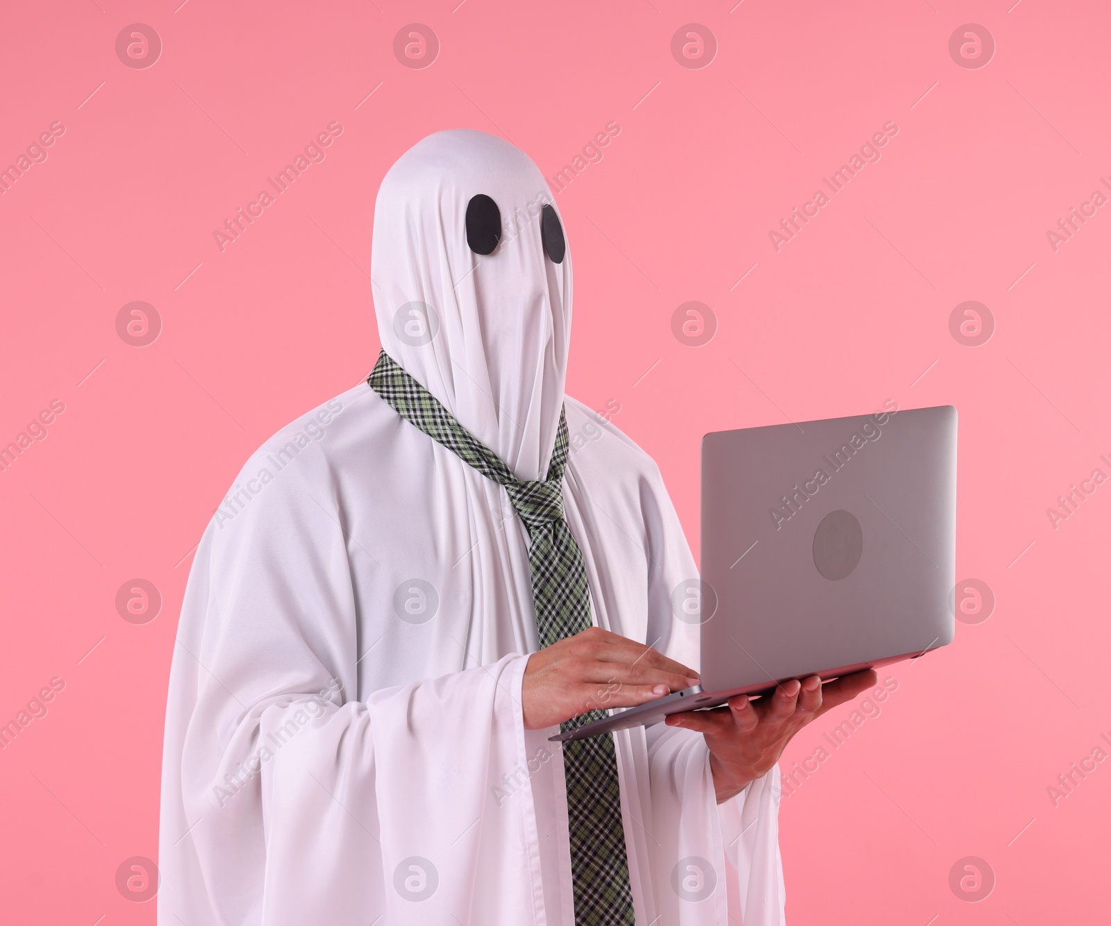 Man in ghost costume using laptop on pink background Photo of Man in ghost costume using laptop on pink background