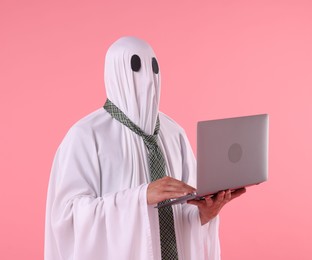 Photo of Man in ghost costume using laptop on pink background