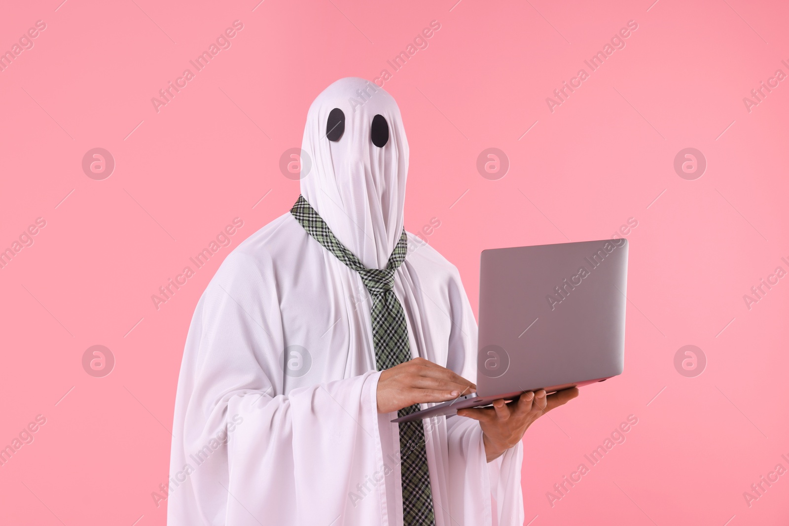 Photo of Man in ghost costume using laptop on pink background