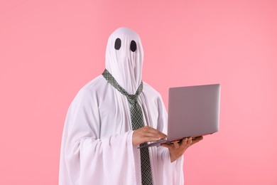 Photo of Man in ghost costume using laptop on pink background