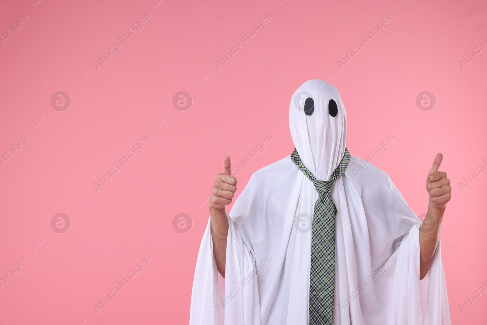 Photo of Man in ghost costume with tie showing thumbs up on pink background. Space for text