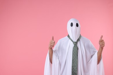 Photo of Man in ghost costume with tie showing thumbs up on pink background. Space for text