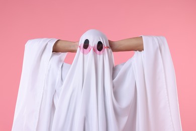 Photo of Cute ghost. Man covered with white sheet in sunglasses on pink background