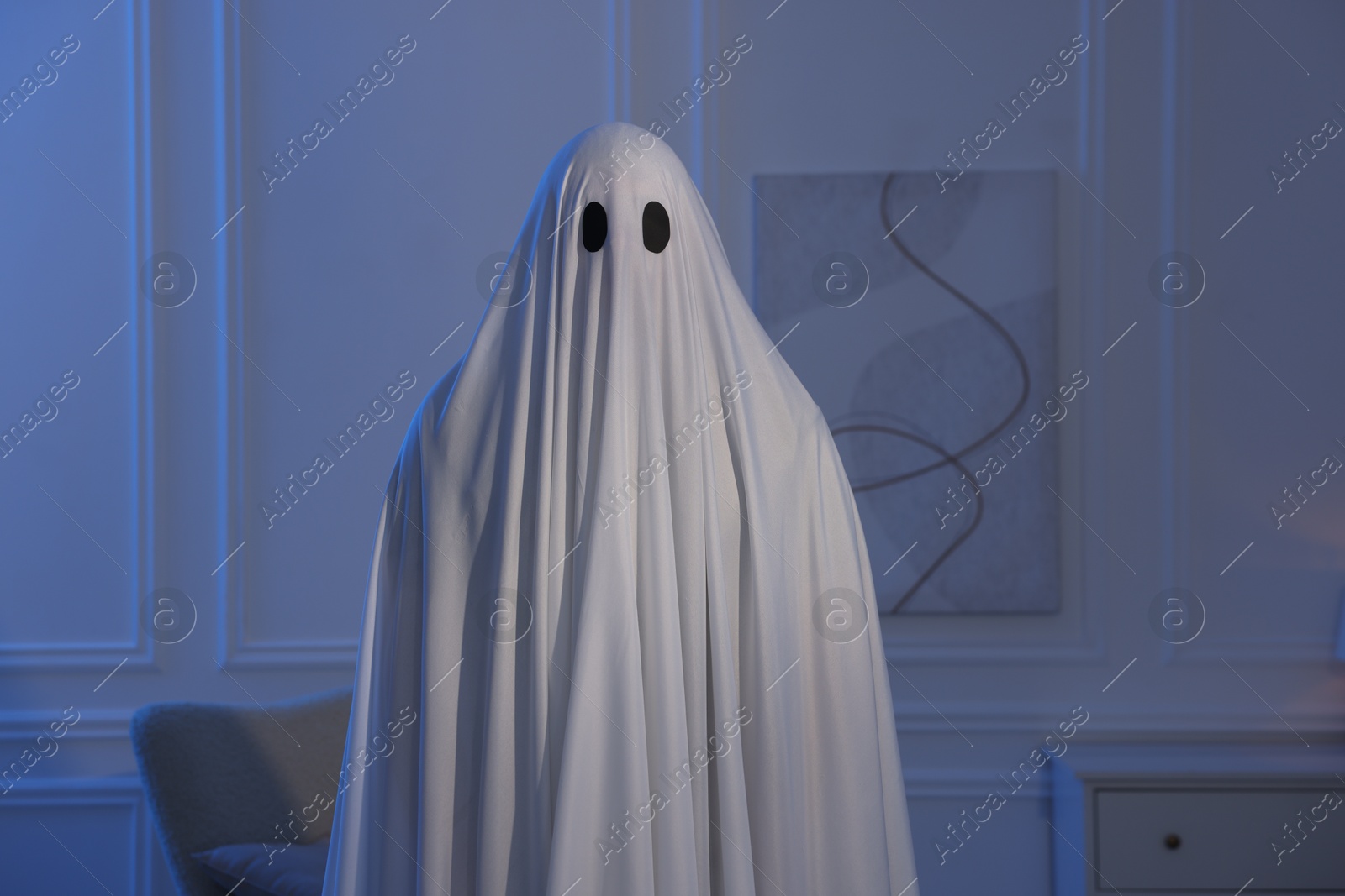 Creepy ghost. Man covered with white sheet in blue light at home Photo of Creepy ghost. Man covered with white sheet in blue light at home