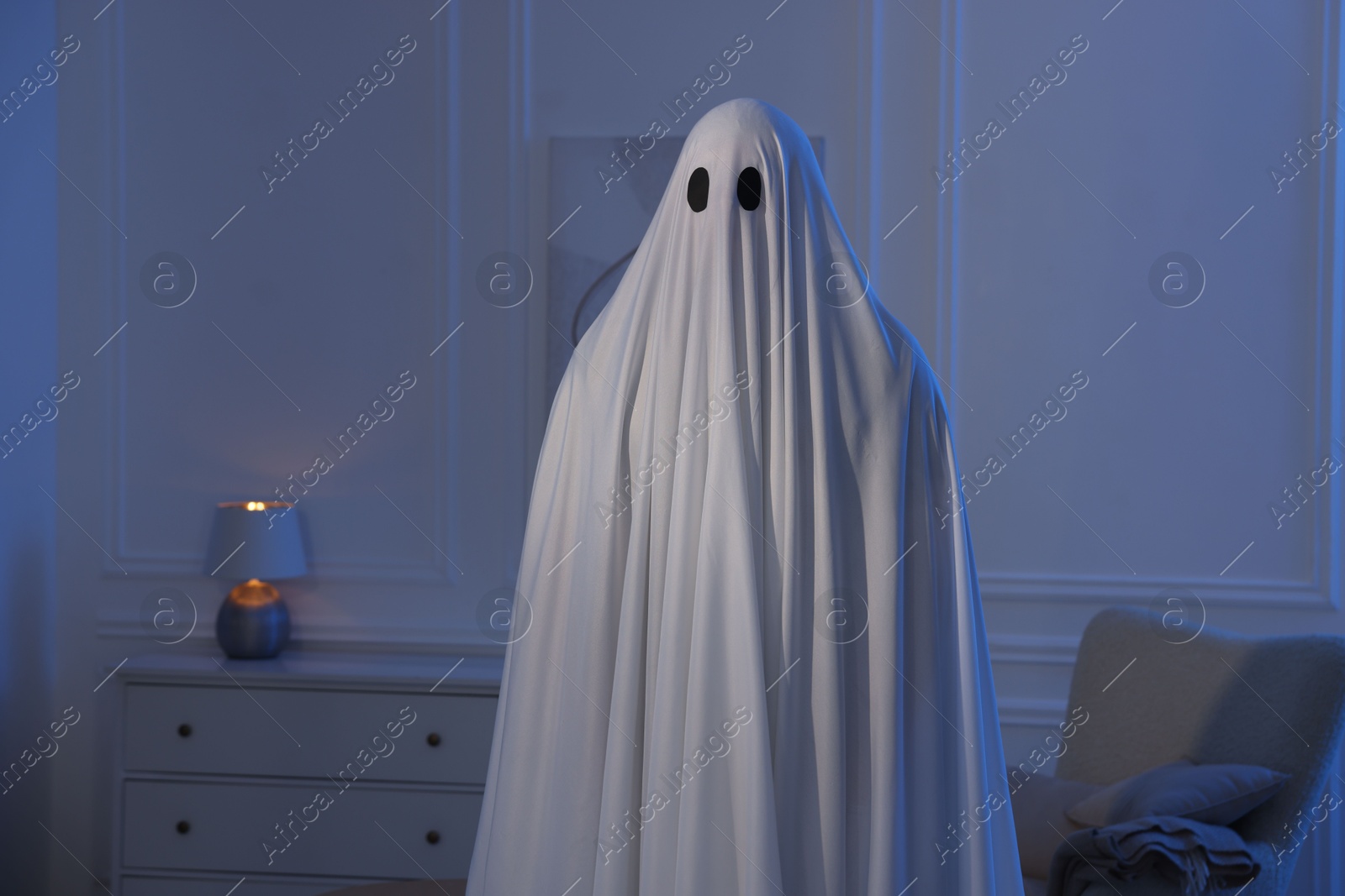 Creepy ghost. Man covered with white sheet in blue light at home Photo of Creepy ghost. Man covered with white sheet in blue light at home