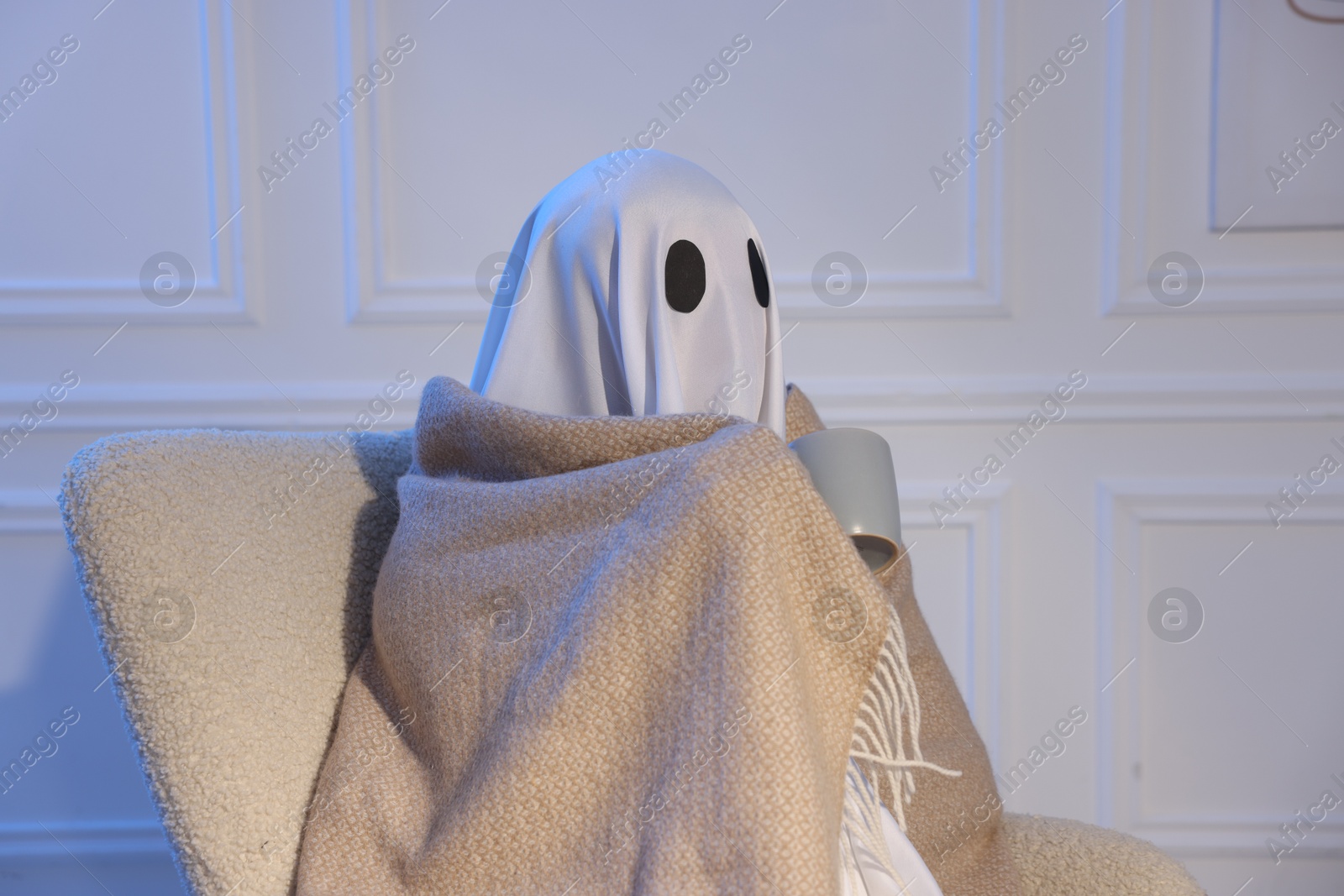 Man in ghost costume wrapped with blanket holding cup of drink at home Photo of Man in ghost costume wrapped with blanket holding cup of drink at home