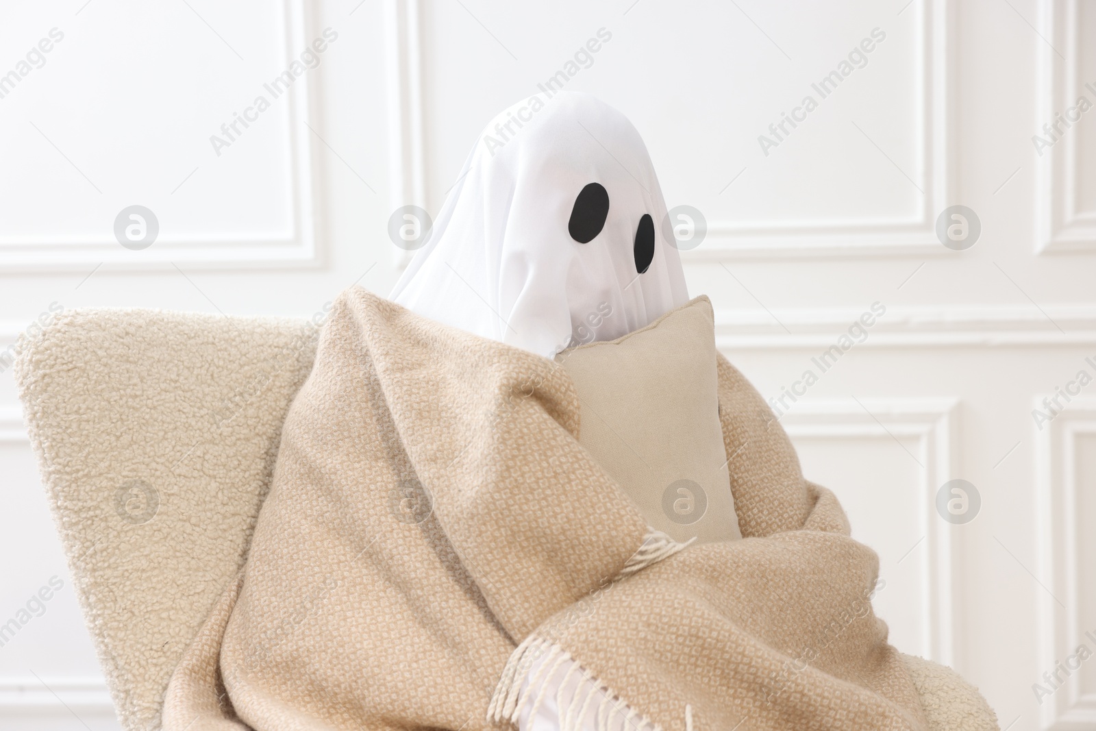 Photo of Man in ghost costume wrapped with blanket holding pillow at home
