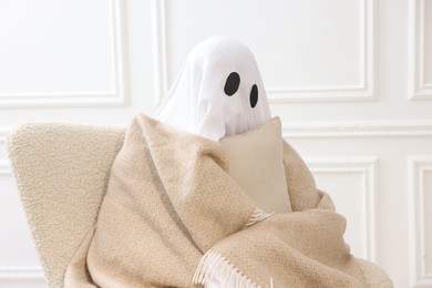 Photo of Man in ghost costume wrapped with blanket holding pillow at home