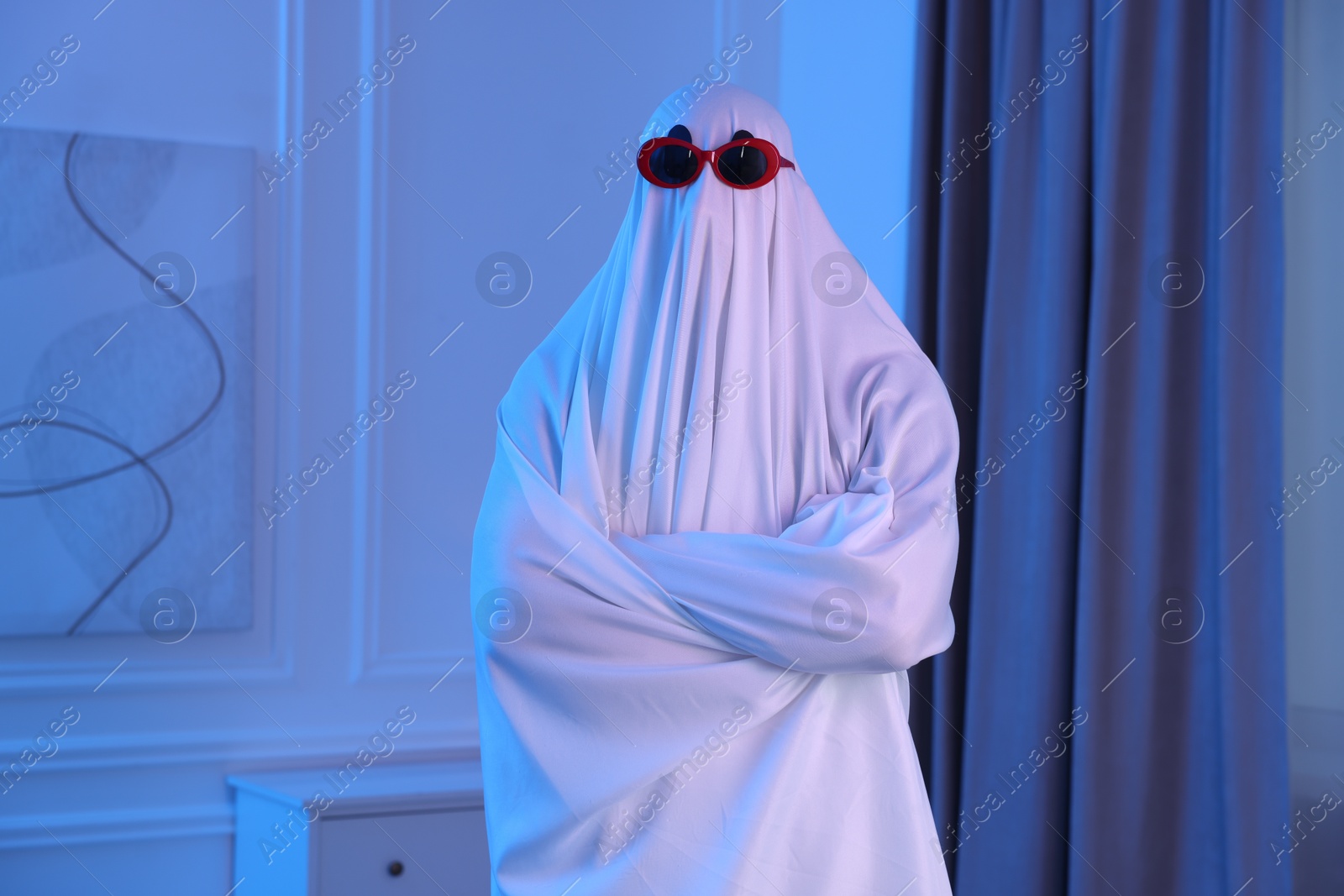 Funny ghost. Man covered with white sheet in blue light at home Photo of Funny ghost. Man covered with white sheet in blue light at home