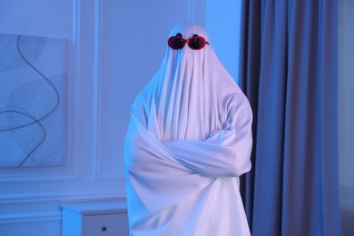 Photo of Funny ghost. Man covered with white sheet in blue light at home