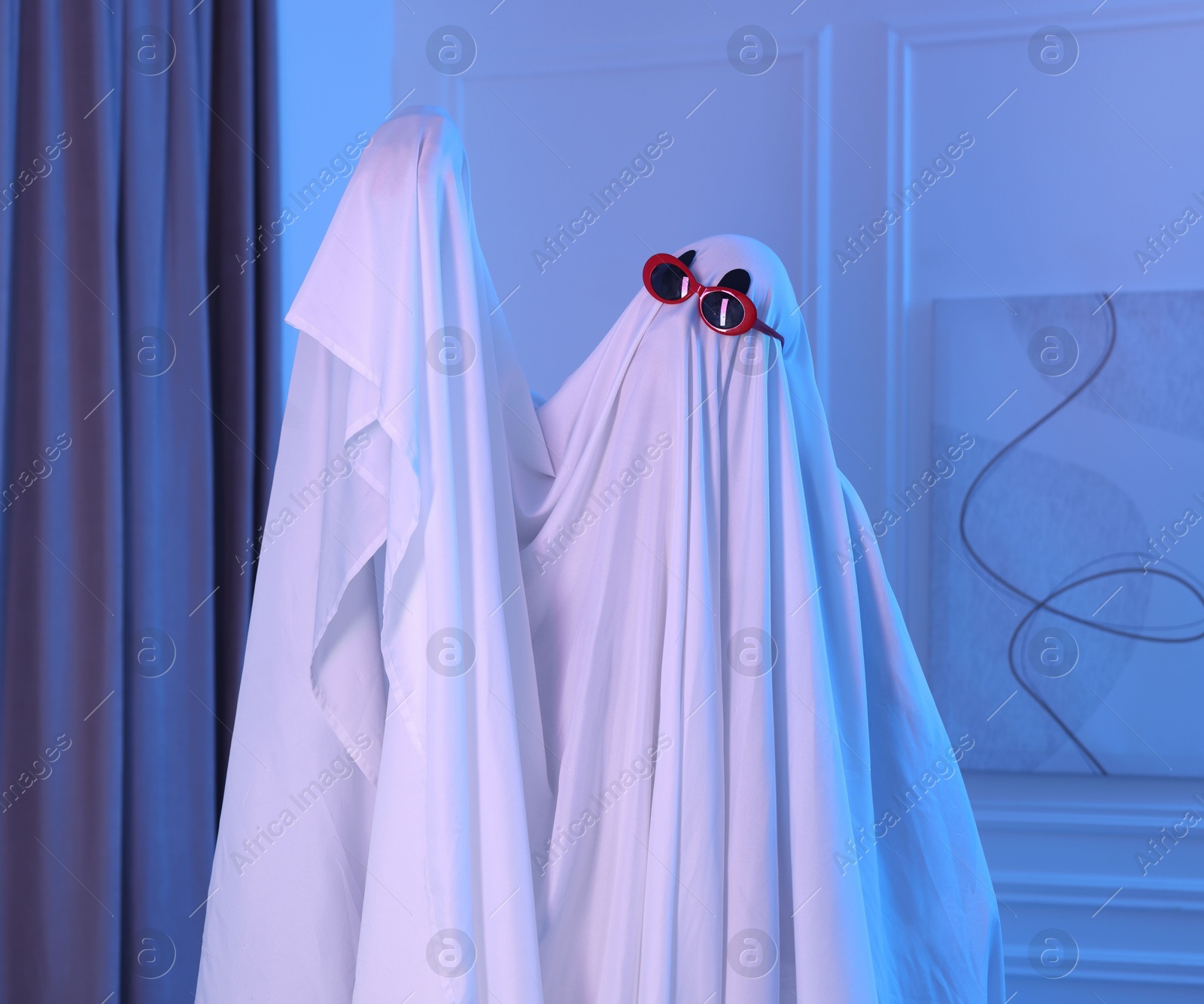 Funny ghost. Man covered with white sheet in blue light at home Photo of Funny ghost. Man covered with white sheet in blue light at home